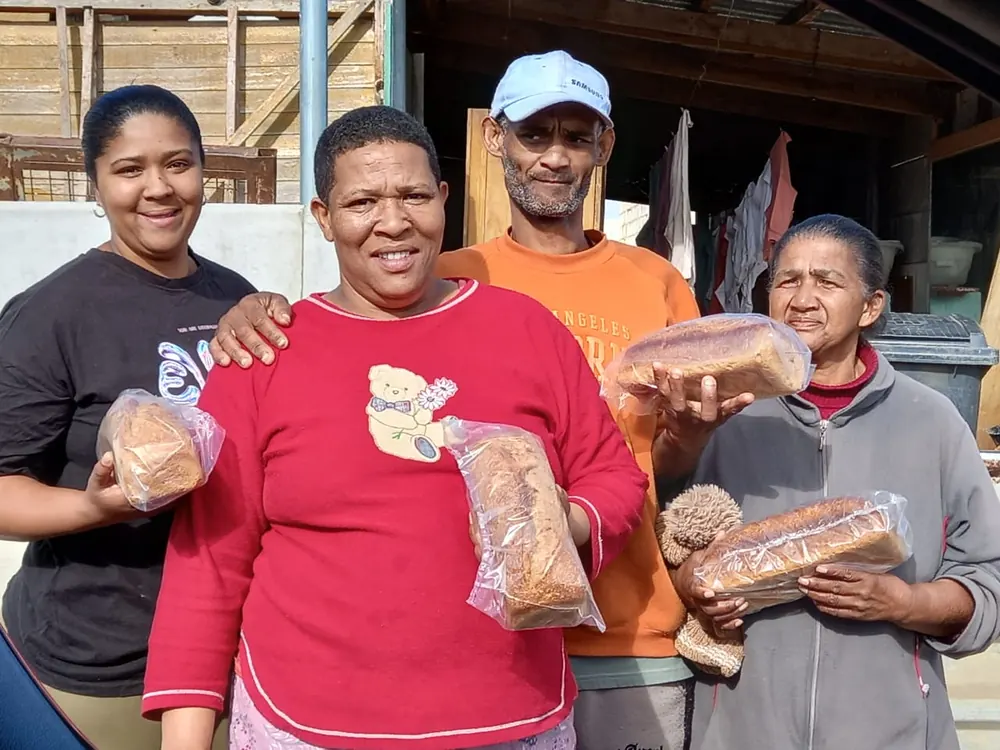Four neighbours hold their loaves of bread