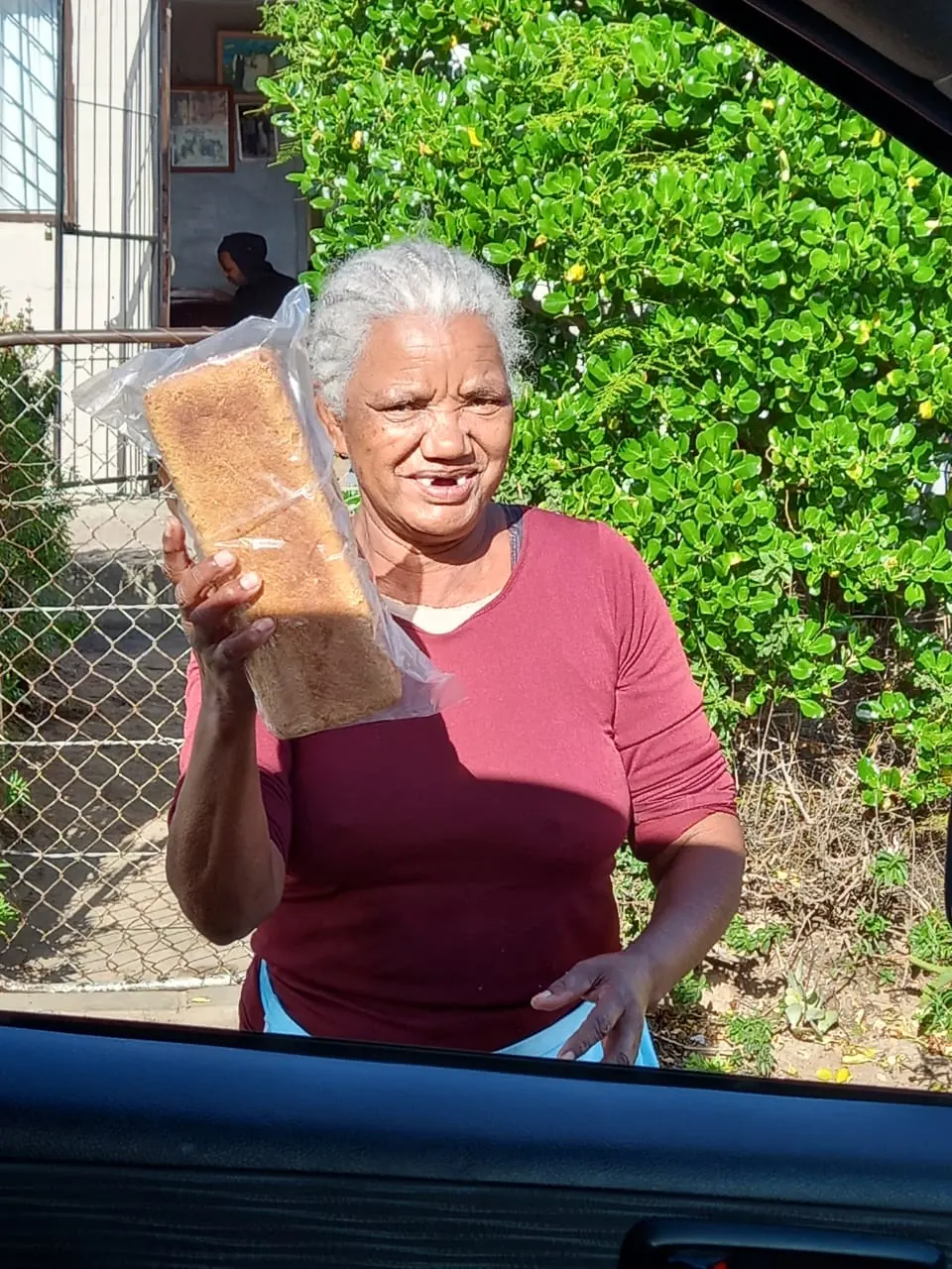A grandmother smiles as she holds up her loaf of bread